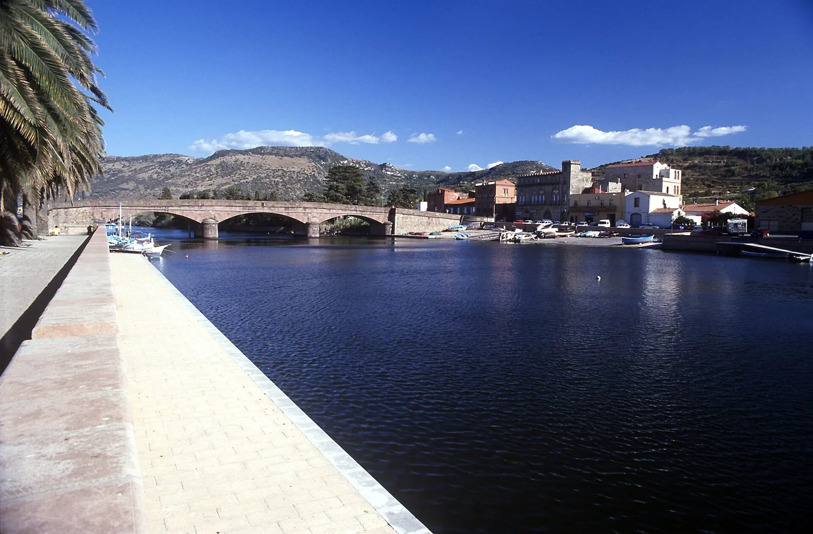 Il lungofiume del Temo a Bosa con il ponte vecchio in pietra e le colline sullo sfondo