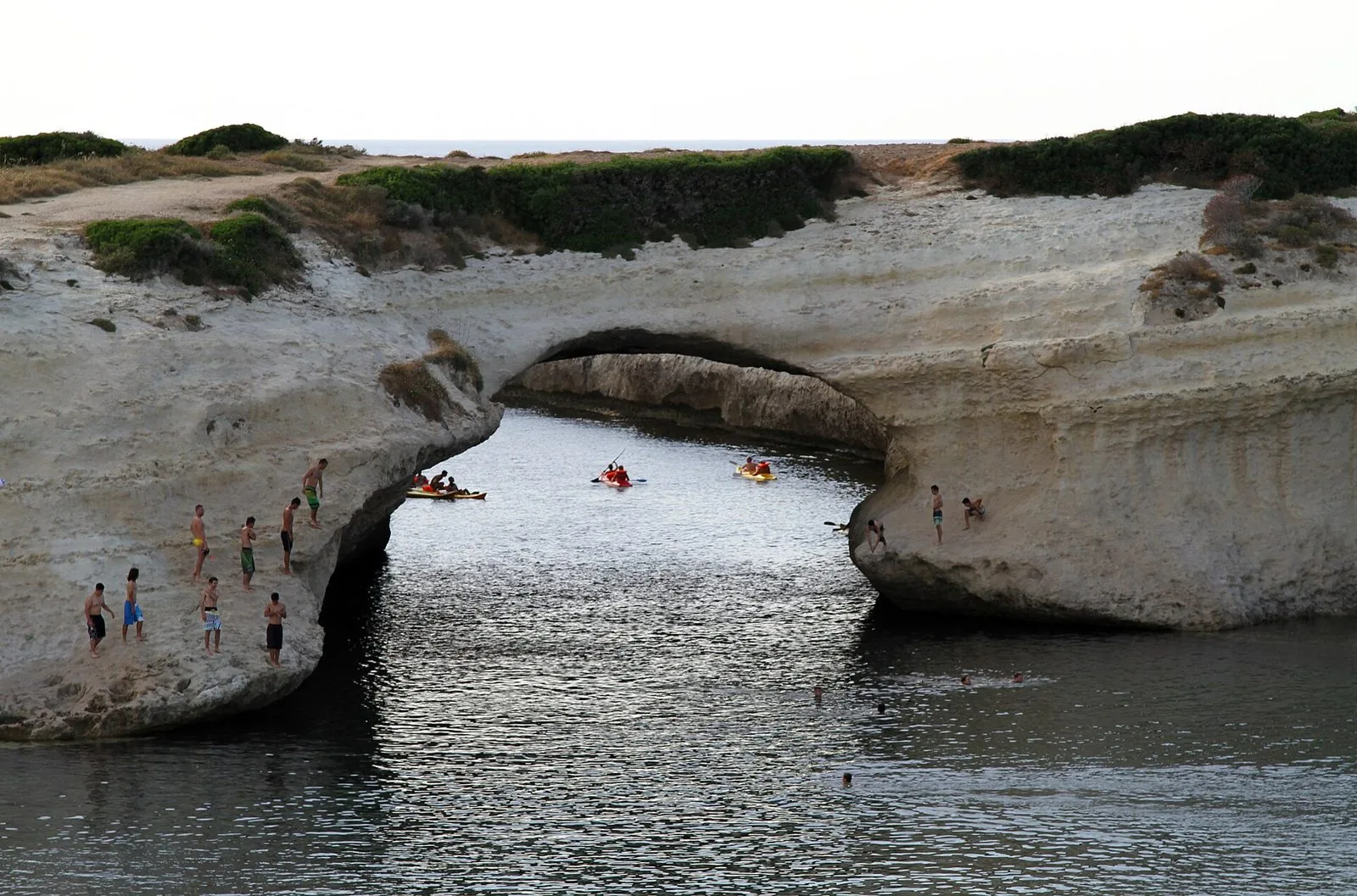 L'arco naturale di roccia calcarea di S'Archittu che si apre sul mare calmo, con canoe nell'insenatura