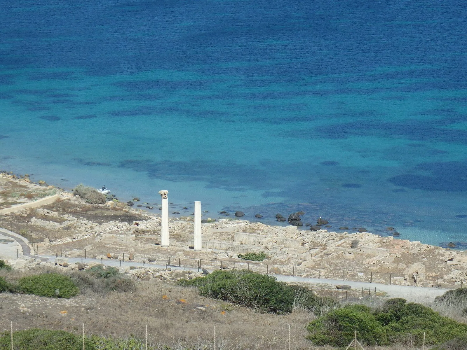 Le due colonne del tempio romano di Tharros tra le rovine, con il mare turchese sullo sfondo